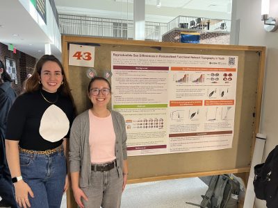 Jillian O'Malley dressed in a penguin costume and Heather Robinson dressed in a hippo costume standing by a science poster with text and charts